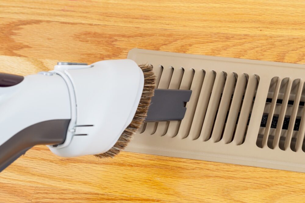 Vacuum being used to clean dust out of air vent for home HVAC system with heat pump